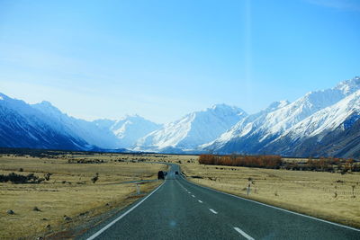 Empty road leading towards snowcapped mountains against sky