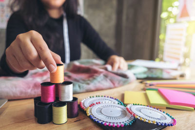 Midsection of fashion designer stacking colorful thread spools on table