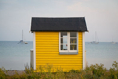 Yellow house on beach by sea against sky