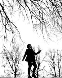 Playful young woman walking by bare trees against sky