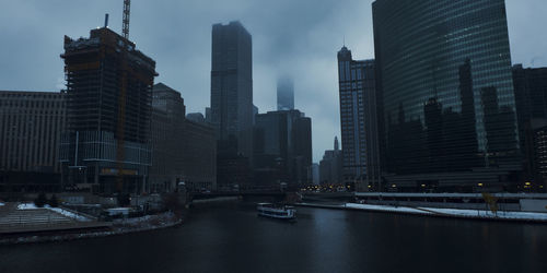 Modern buildings by river against sky in city