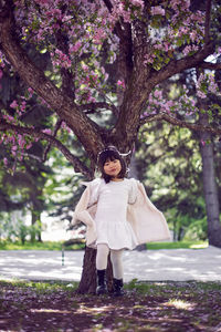 Korean girl in a white light fur coat and a headband stands in a garden with cherry blossoms