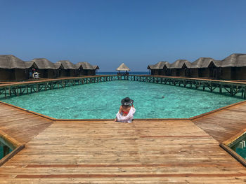 Woman sitting by swimming pool against blue sky