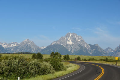 Scenic view of road by mountains against clear blue sky