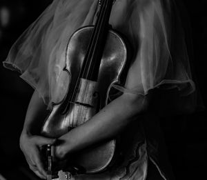 Midsection of woman holding violin against black background