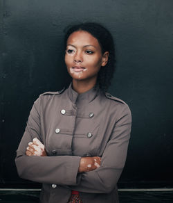 Thoughtful woman with arms crossed suffering from vitiligo standing against wall