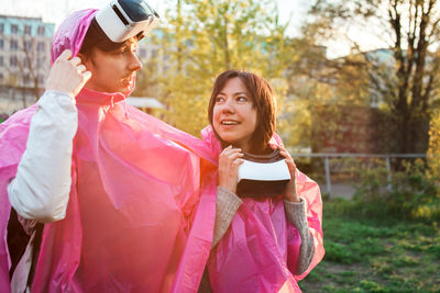 Happy young couple wearing raincoat and virtual reality simulator at park