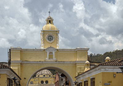 Low angle view of clock tower el arco amidst buildings in city la antigua guatemala.