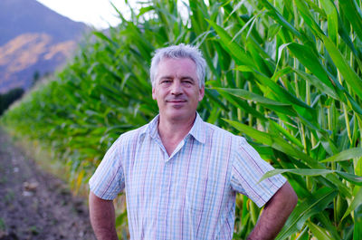 Portrait of smiling mature farmer standing against plants