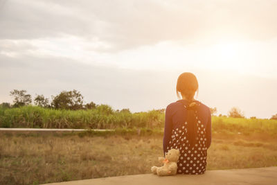 Rear view of man sitting on field against sky