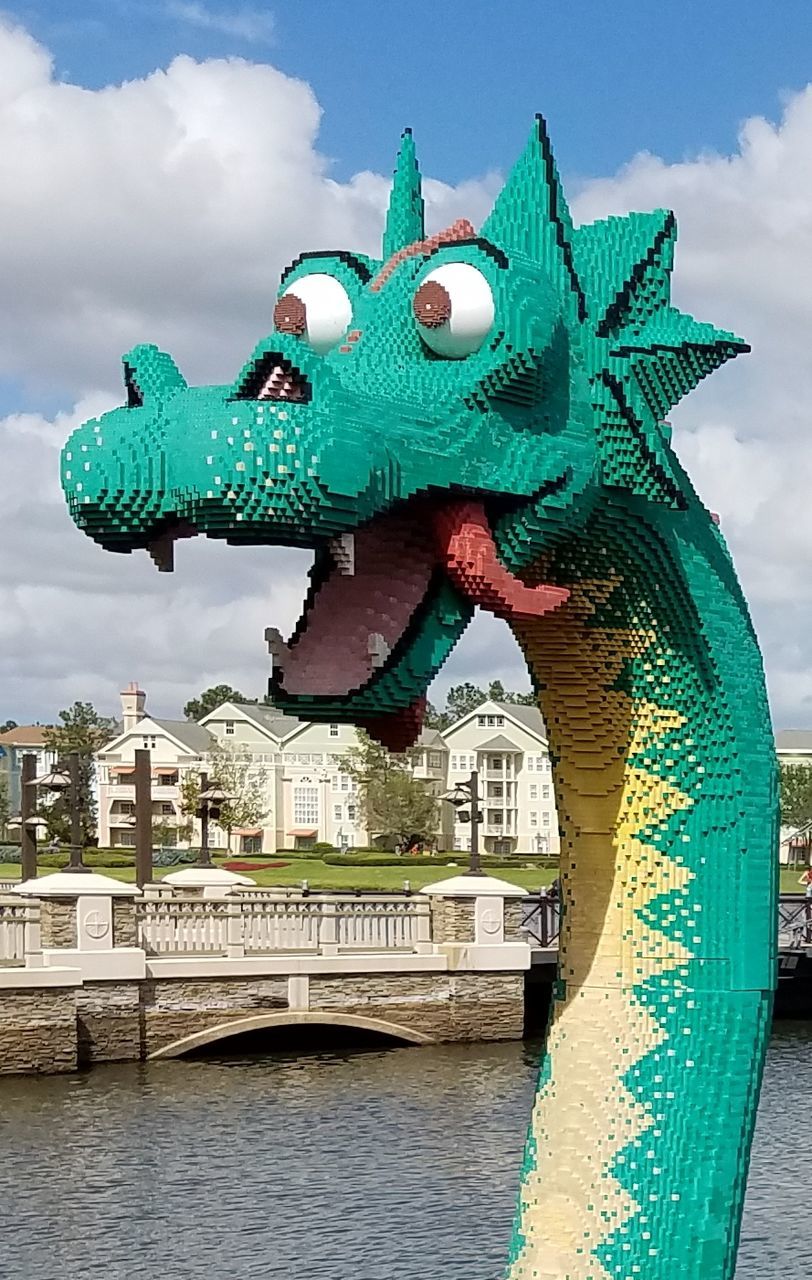 animal representation, art and craft, water, sculpture, cloud - sky, sky, statue, architecture, built structure, outdoors, river, green color, day, no people, building exterior, dragon