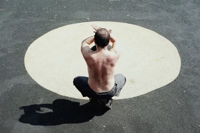 Rear view of shirtless man exercising at playground during sunny day