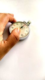 Close-up of hand holding clock against white background