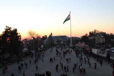 People on street amidst buildings in city against sky during sunset