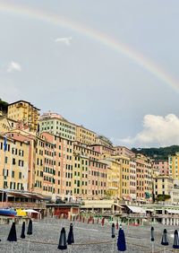 People on rainbow over buildings in city against sky