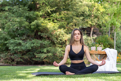 Young beautiful woman in activewear meditating in yoga pose in nature landscape with afternoon light