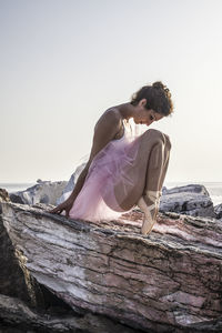 Full length of ballet dancer sitting on rock against clear sky