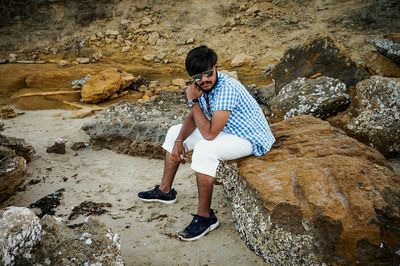 Portrait of young man sitting on rock at beach