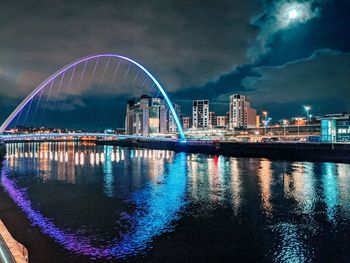 Illuminated city by river against sky at night