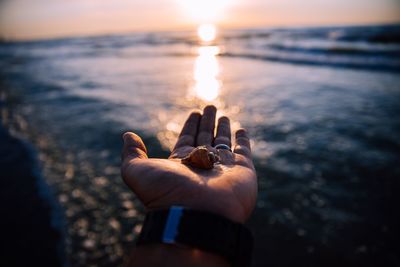 Midsection of person hand on sea shore during sunset