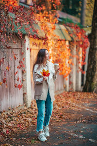 Woman holding umbrella standing by autumn leaves