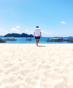 Rear view of man walking at beach against sky