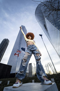 Woman with hand raised standing on concrete seat in city