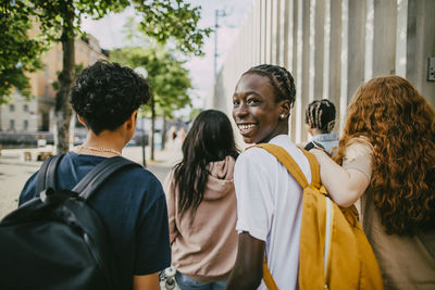 Portrait of happy teenage boy looking over shoulder while walking with friends in city