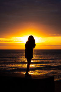 Silhouette woman looking at sea against sky during sunset