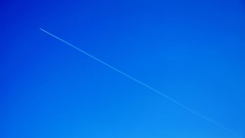 Low angle view of vapor trails against clear blue sky