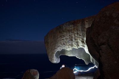 Rock formation by sea against sky at night