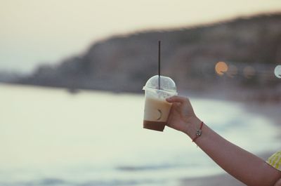 Cropped hand of person holding coffee in disposable cup at beach