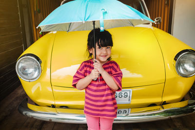 Portrait of smiling girl holding umbrella standing by vintage car