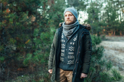 Young man looking away while standing against trees in forest