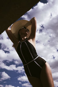 A portrait of a woman in a swimsuit, hat and sunglasses in summer on the riverbank against the sky