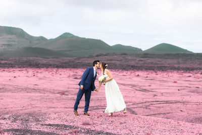 Front view of man and woman standing on volcanic landscape against sky