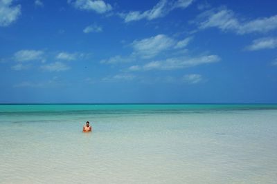 View of woman sitting in the calm sea against blue sky