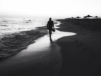 Silhouette man walking on shore at beach against clear sky