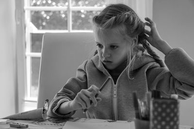 Thoughtful girl sitting by table on chair at home