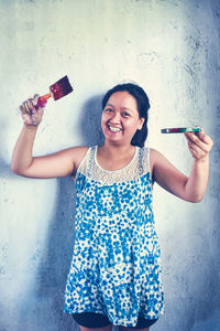 Portrait of a smiling young woman standing against wall