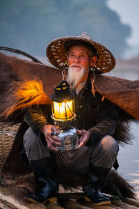 Man holding lantern while sitting on boat in lake