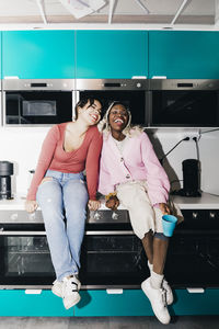 Happy young women sitting on kitchen counter in college dorm