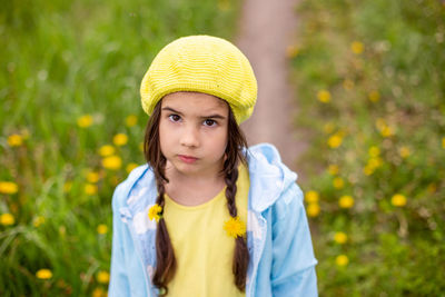 Portrait of a sad adorable little girl with two pigtails in a yellow beret, blue raincoat.