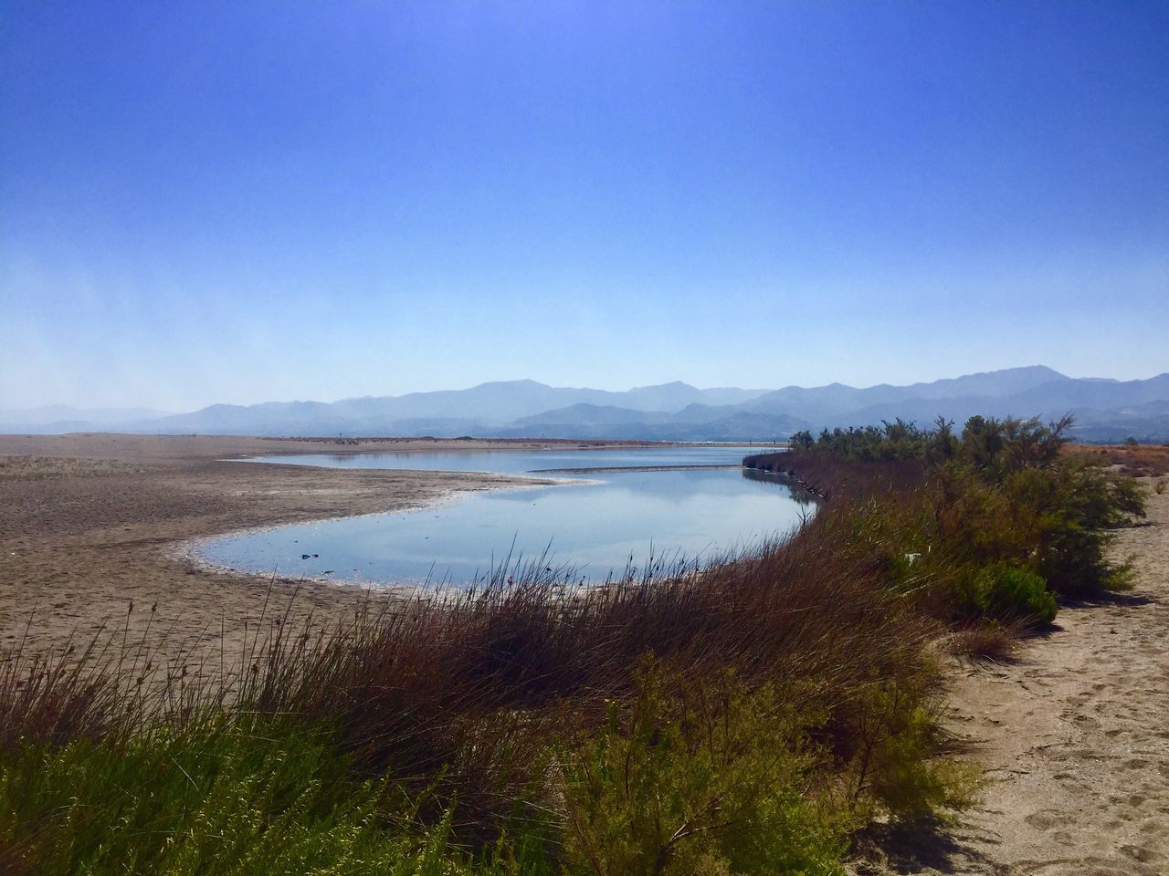 grass, tranquil scene, scenics, mountain, nature, water, tranquility, landscape, beauty in nature, outdoors, lake, mountain range, no people, travel destinations, day, blue, sky, clear sky