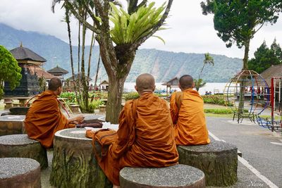 Rear view of men sitting on mountain against sky