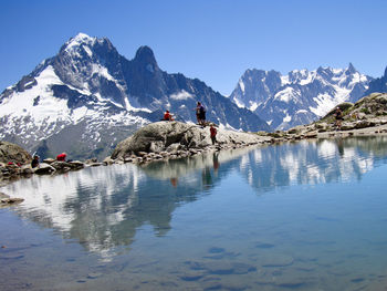 People on snowcapped mountains by lake against clear blue sky