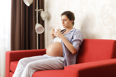 Side view of woman using mobile phone while sitting on sofa at home