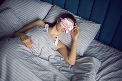 Woman in a pink eye mask lies under a blanket in a bed and suffers from insomnia
