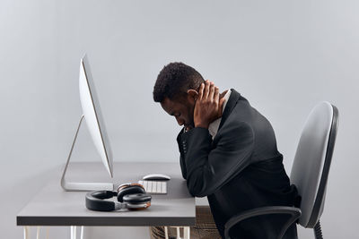 Side view of young man using laptop while standing against white background