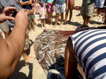 High angle view of people standing by fish in fishing net at beach